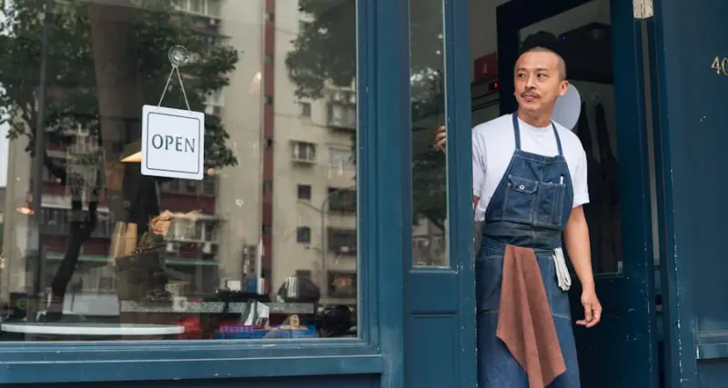 Small business owner standing by an open shop sign